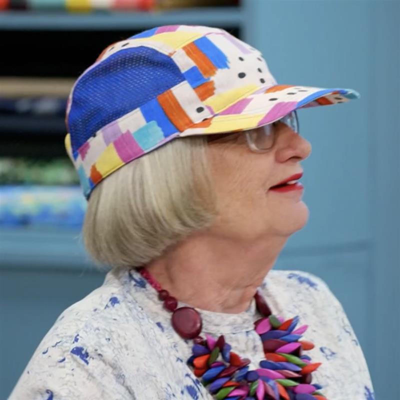 Esme, Person wearing a colorful hat and necklace against a blurred background