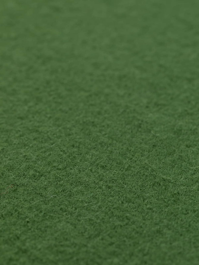 Angled close-up of Croquet Lawn Green boiled wool fabric laid flat, highlighting its soft green shade with calming grey undertones and plush texture, perfect for creating sophisticated, natural fibre clothing from our UK ecommerce store.