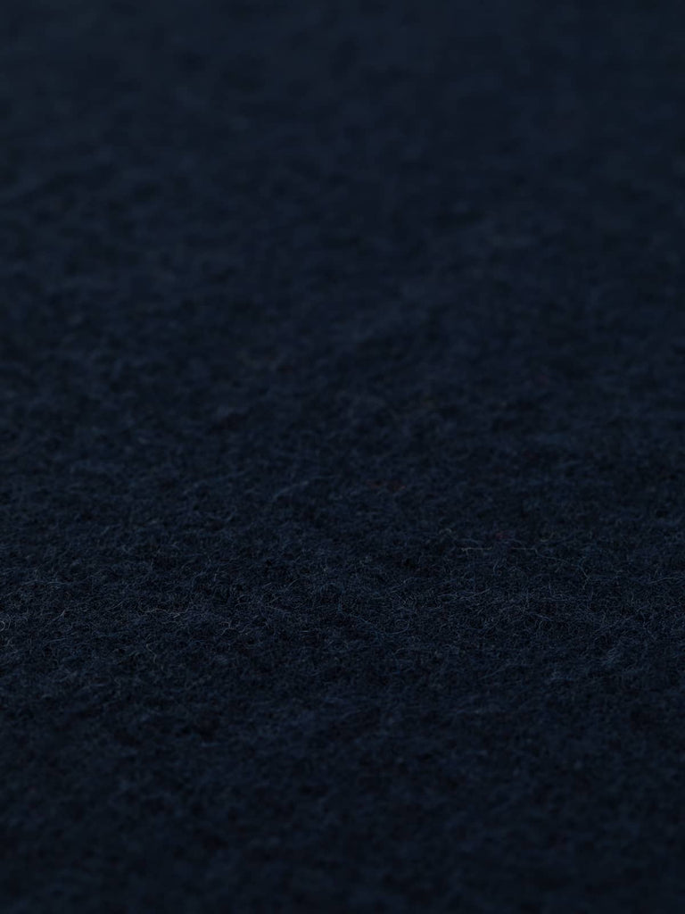 Angled close-up of Total Eclipse boiled wool fabric laid flat, highlighting its dark navy color and soft, textured finish. A classic choice for stylish and reliable pieces—order today for your next sewing project.