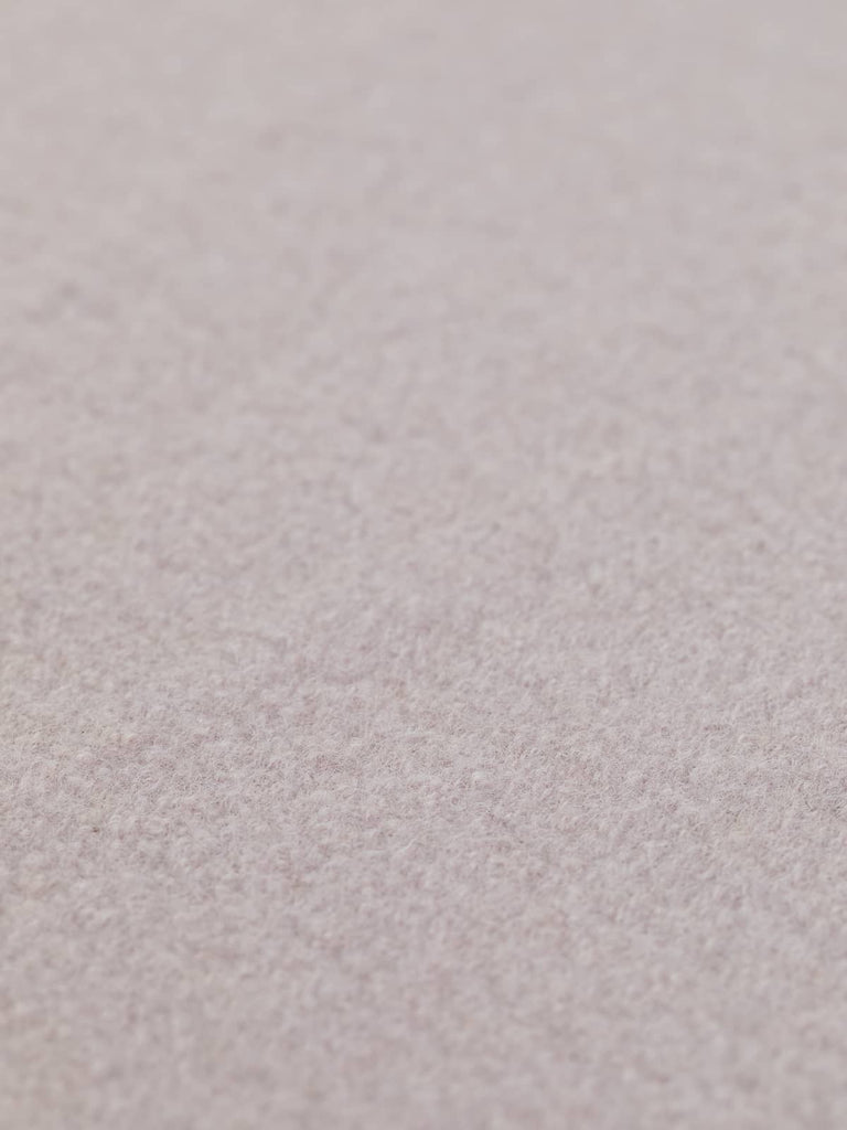 Angled close-up of Lunar Pink boiled wool fabric laid flat, highlighting its pastel pink and lilac tones with a soft, textured finish. Elevate your creations with this exquisite fabric—order today for your next project.