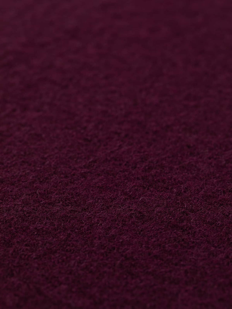 Angled close-up of Plum Wine boiled wool fabric laid flat, showcasing its opulent jewel-like tones and plush texture, perfect for adding a touch of luxury to your wardrobe with natural fibre clothing from our UK ecommerce store.