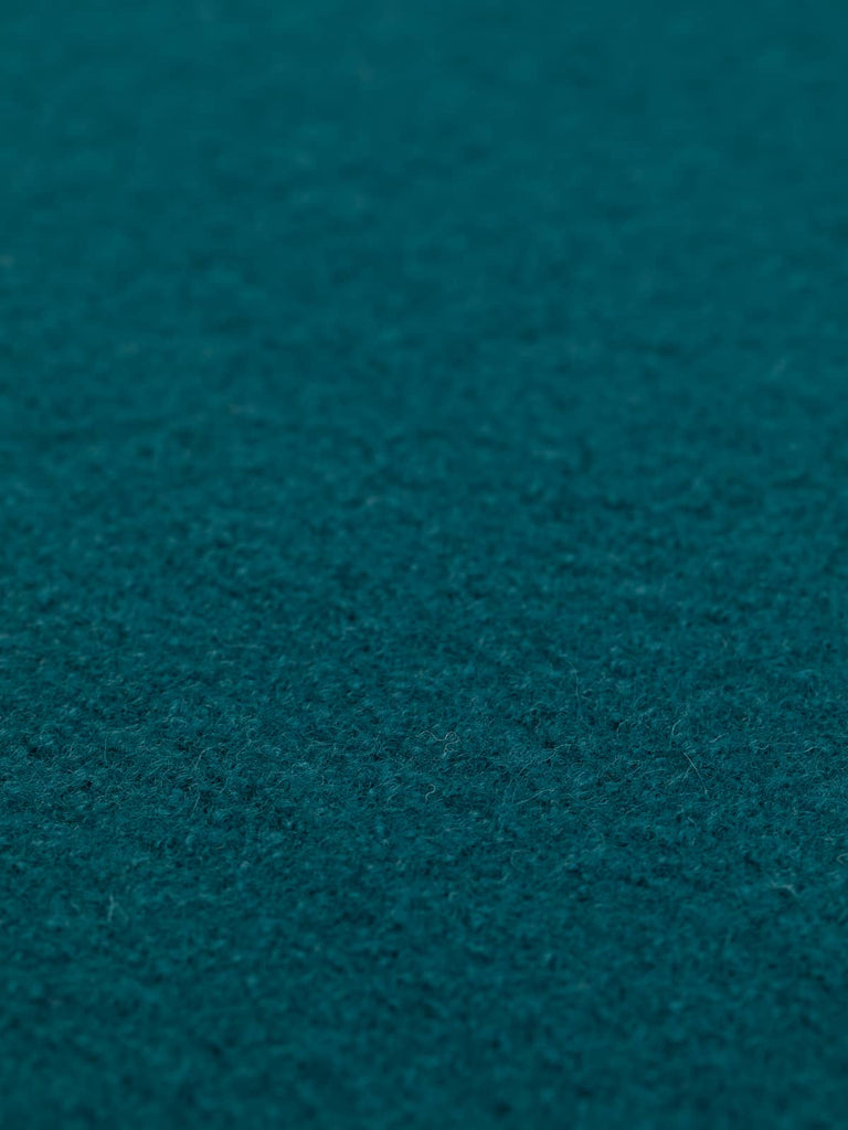 Angled close-up of Classic Teal boiled wool fabric laid flat, showcasing its deep, iridescent blue-green color. Bring a touch of nature's beauty to your designs—order this versatile fabric now.