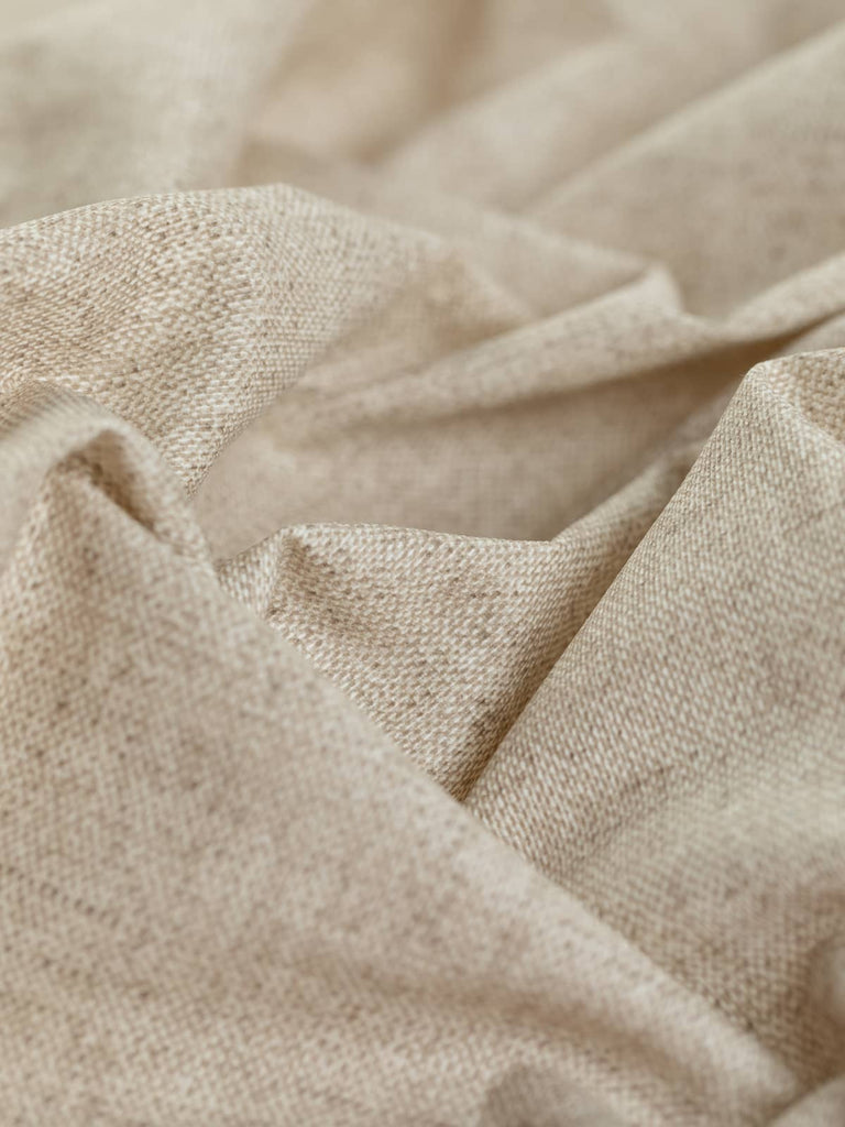 A close-up view of the Waterproof Outdoor Furnishing Fabric - Oatmeal Speckle, twisted to showcase its lightly textured surface. The warm multi-tones of beige form a rustic oatmeal basket weave design, while the light vinyl-basket-like texture, due to the acrylic coating, highlights its water-resistant properties. The 50% cotton and 50% polyester blend provides a strong and stable fabric with a slightly crisp hand. Perfect for various outdoor furnishing needs.