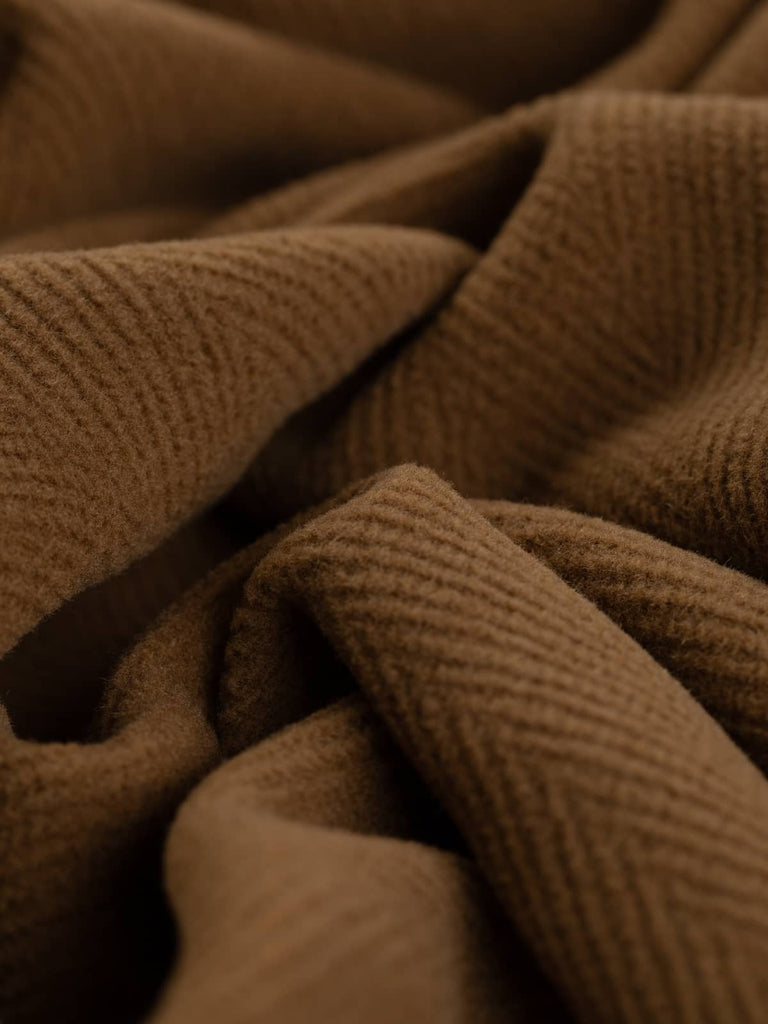 Detailed shot of Italian-made wool fabric in a rich tan hue, highlighting the prominent jumbo herringbone pattern. This versatile fabric is perfect for tailored overcoats, historical costumes, or luxurious upholstery.