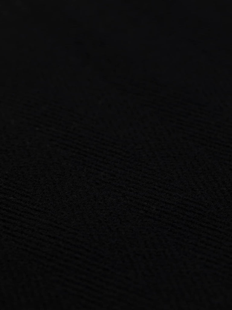 Close-up of coal-black wool fabric featuring bold 6cm herringbone chevrons. This heavyweight 100% wool fabric offers a timeless, serious tone, perfect for overcoats, corporate uniforms, and upholstery.