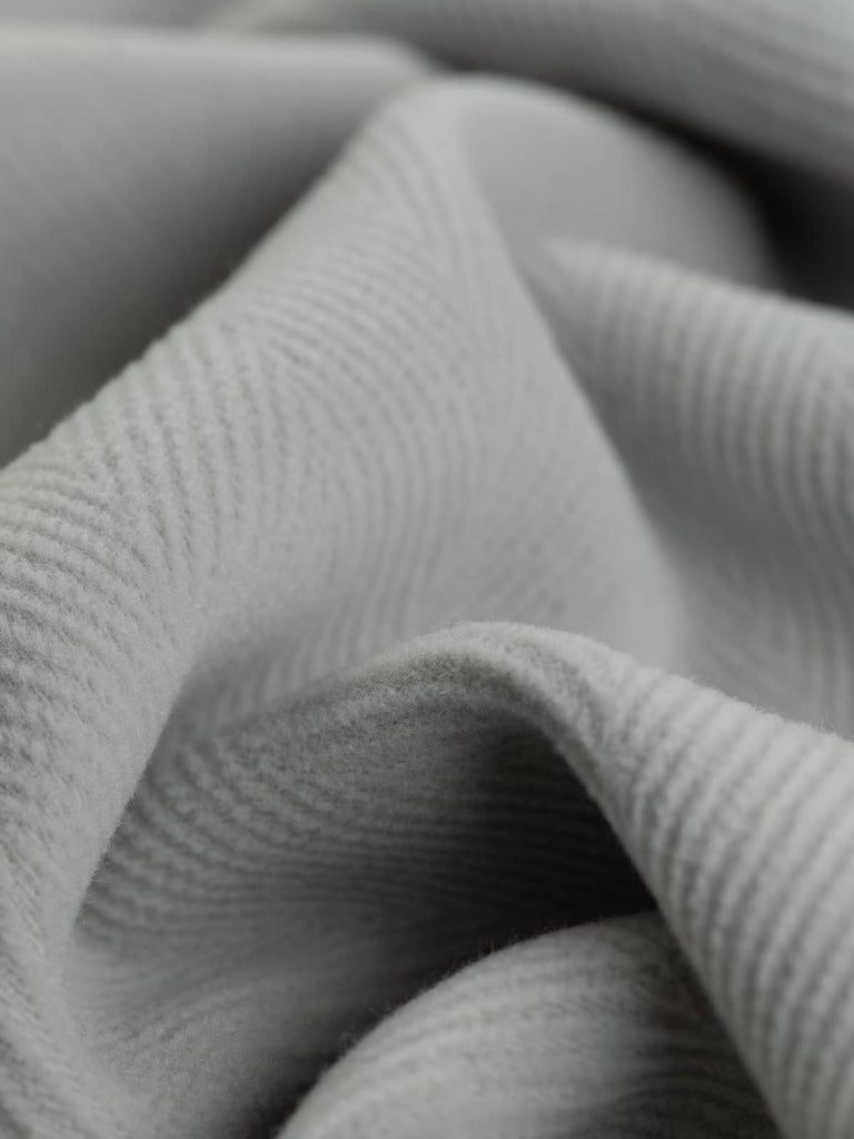 Detailed shot of Italian-made wool fabric in a sleek light grey hue, highlighting the 6cm herringbone pattern. This luxurious fabric is perfect for chic overcoats, durable workwear, and classic home decor like seat cushions or footstools.