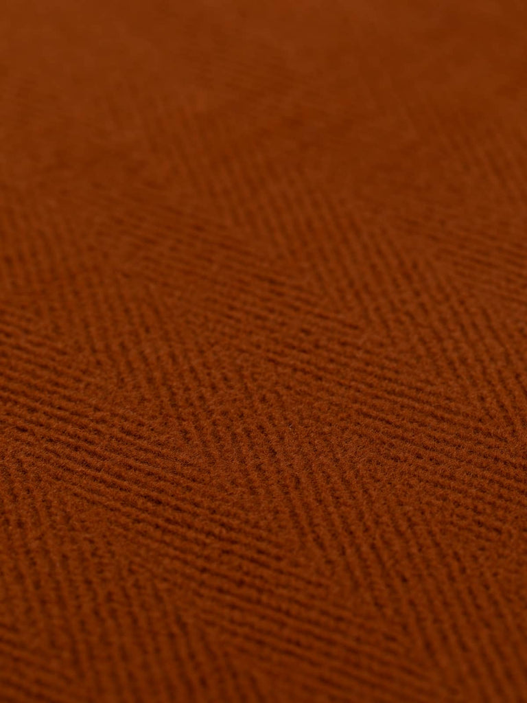 A close-up of rust-colored wool fabric featuring a prominent 6cm herringbone pattern. This heavyweight 100% wool fabric evokes autumnal warmth, perfect for creating cozy overcoats, stylish jackets, or unique home decor pieces like cushions.