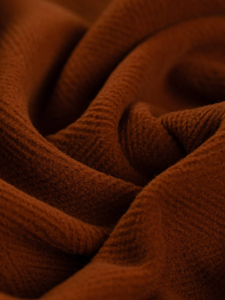 Detailed shot of Italian-made wool fabric in a warm rust hue, highlighting the striking 6cm herringbone weave. This versatile fabric is perfect for chic overcoats, historical costumes, and upscale furnishings, offering both durability and style.