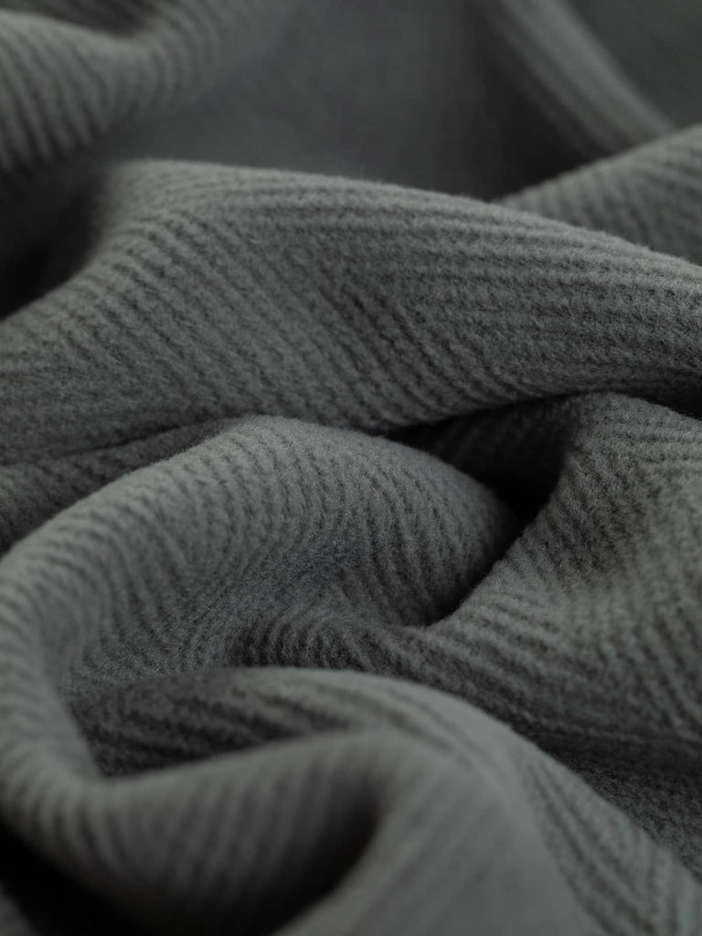 Image highlighting a beautiful mid-grey wool fabric with a distinctive 6cm herringbone weave. This versatile and hard-wearing fabric is suited for chic overcoats, utility-style jackets, and historical costumes, providing a soft yet sturdy drape.