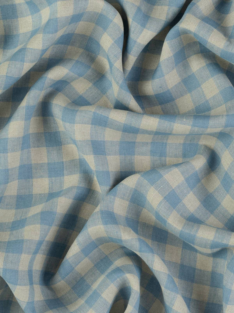Viewed from above, this twisted linen showcases a subtle interplay of earthy beige and washed blue checks. The gentle folds emphasize its light-medium weight and casual drape, perfect for effortless summer styling.