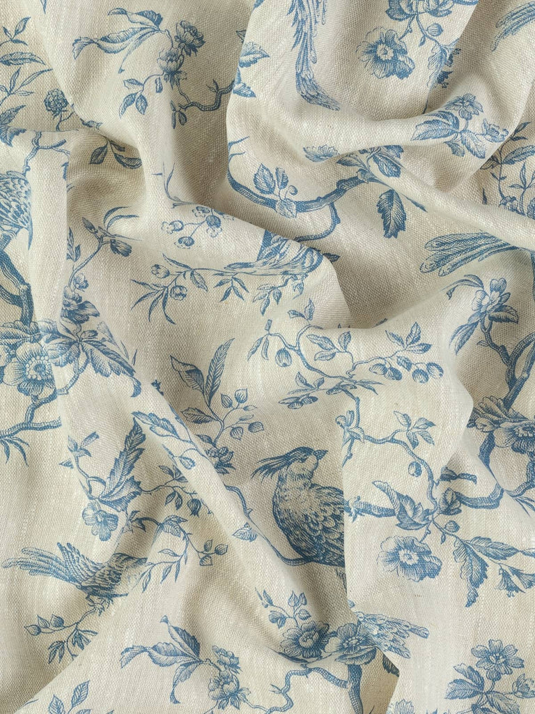 Top-down view of twisted fabric revealing softly textured linen with delicate blue printed birds, berries, and climbing foliage. The gentle twist highlights its classic linen slubs and vintage French charm.