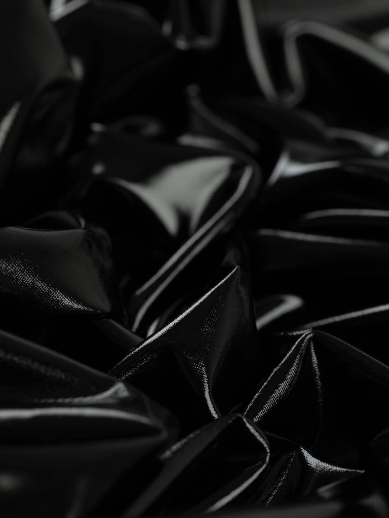 Wet Look PU Coated Jersey in Tar Black, twisted to showcase its fluid drape and glossy finish. This lightweight, stretchy polyester-spandex fabric features a sleek, high-fashion wet look with a smooth, matte jersey reverse. Perfect for form-fitting garments, cosplay, and statement fashion pieces.